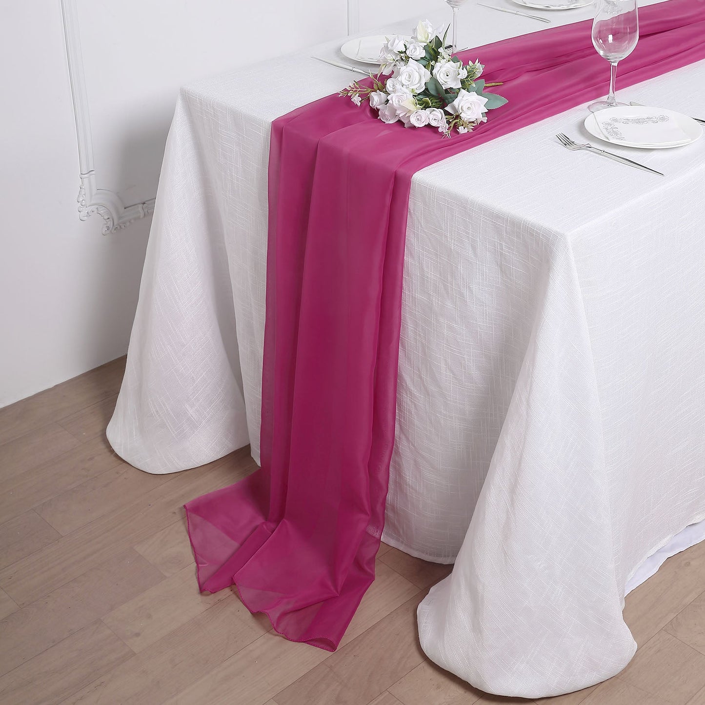 Fuchsia chiffon table runner on a white tablecloth with floral decoration.
