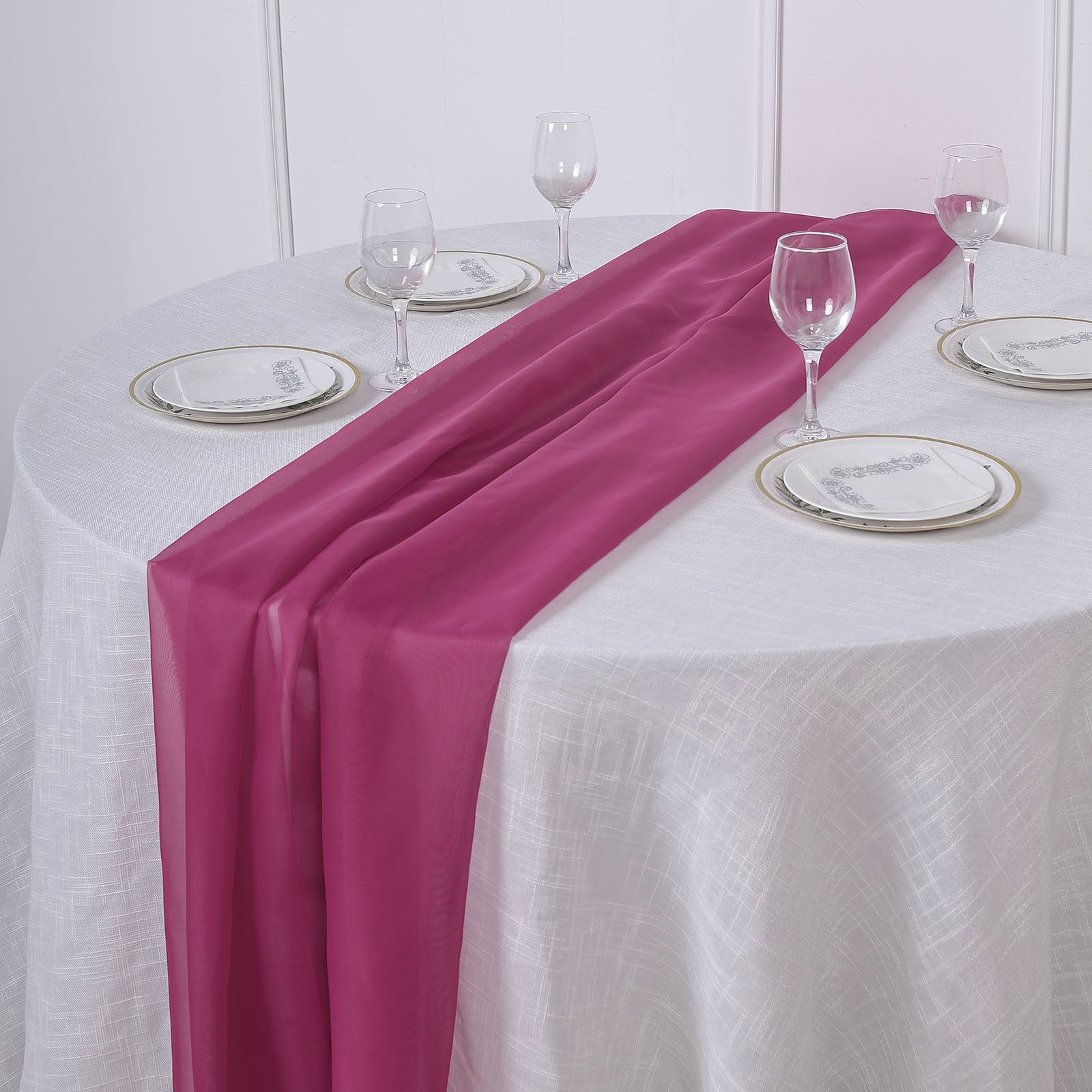 Fuchsia chiffon table runner on a white tablecloth with dinnerware.