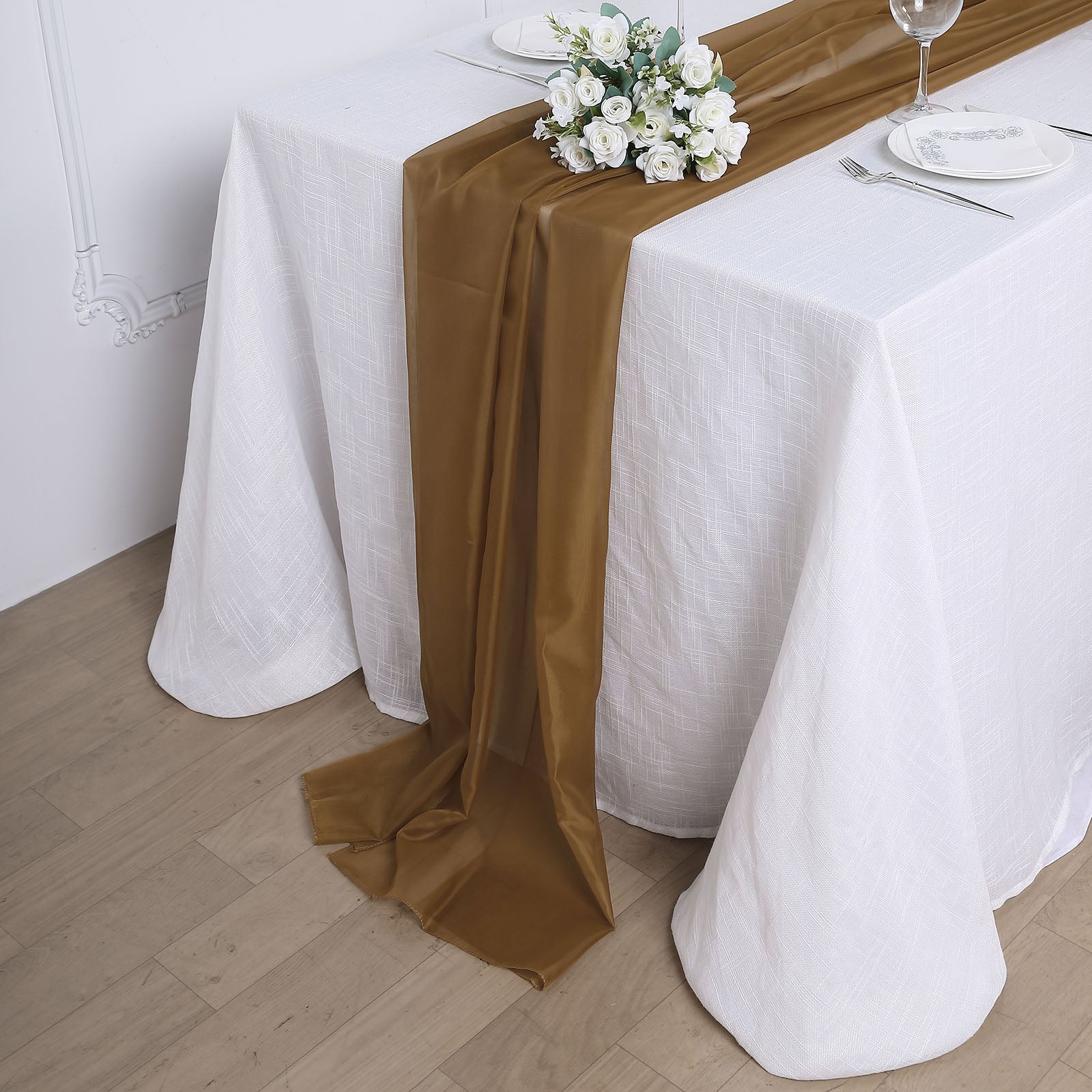 Gold chiffon table runner on a white table with floral centerpiece.