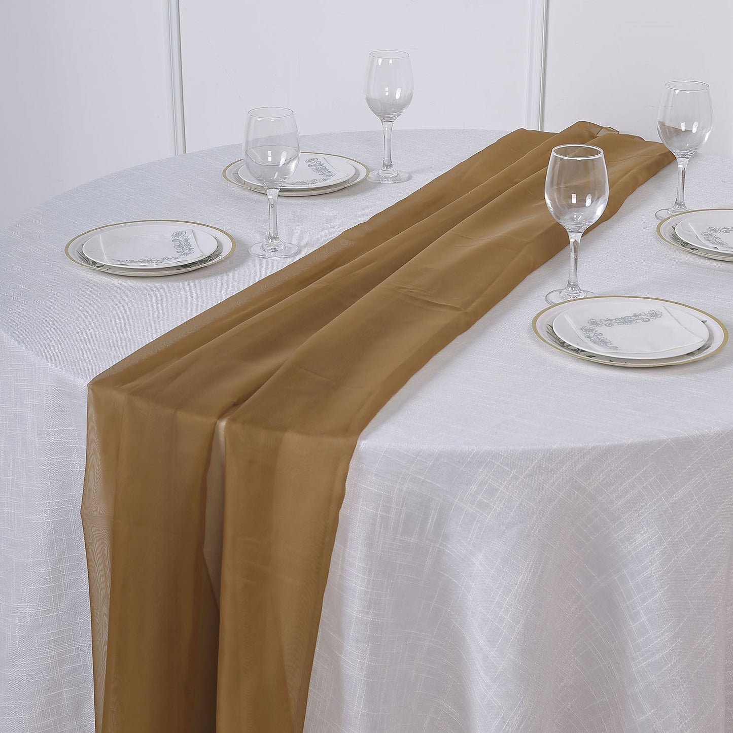 Gold chiffon table runner on a round table set for dining.