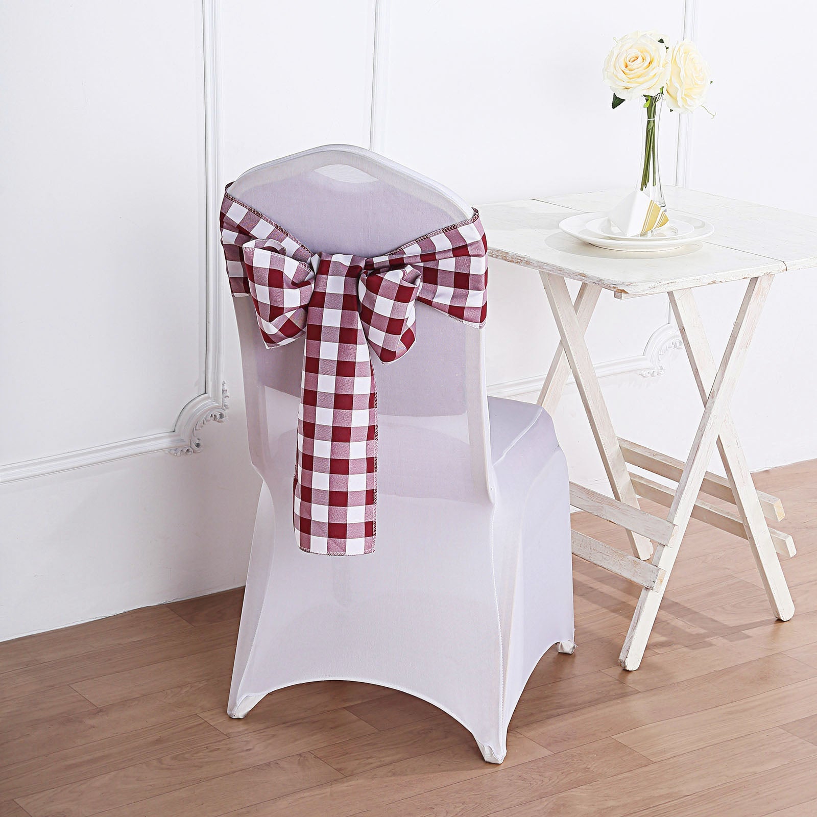 Burgundy and white checkered chair sashes on a white chair.