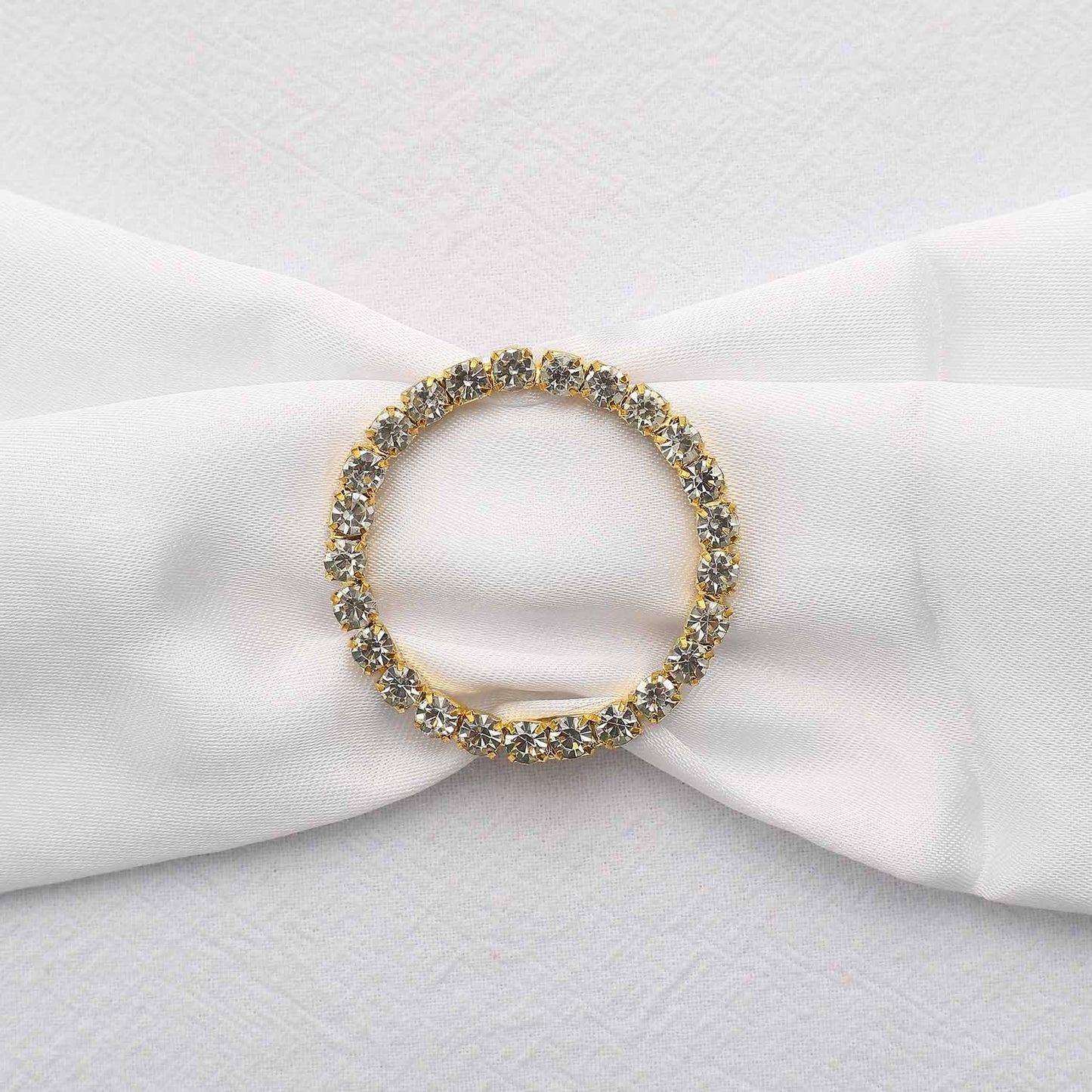 Gold rhinestone circle metal chair sash band buckle on white fabric.