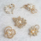 Gold plated pearl and rhinestone floral brooches set on lace background.