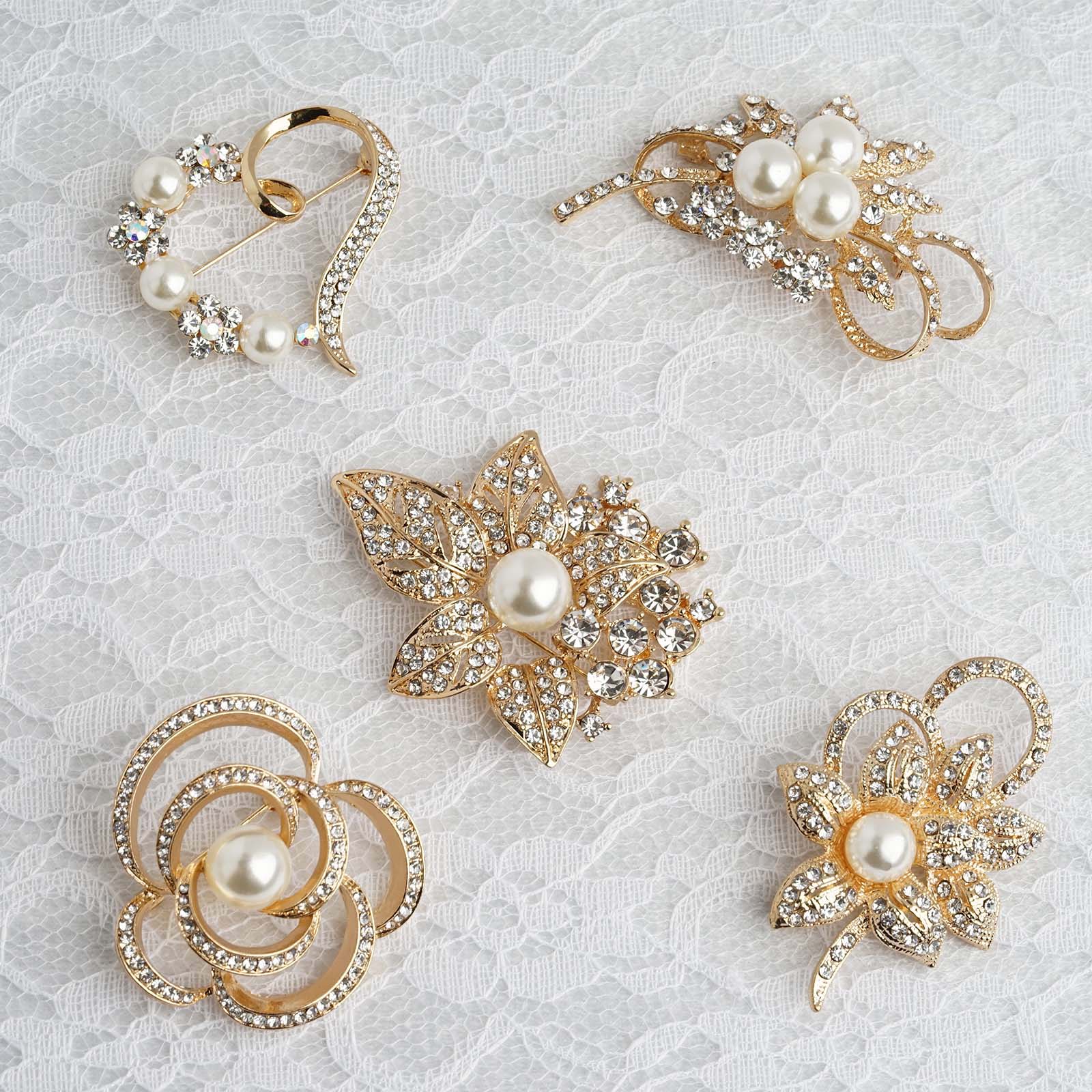 Gold plated pearl and rhinestone floral brooches set on lace background.