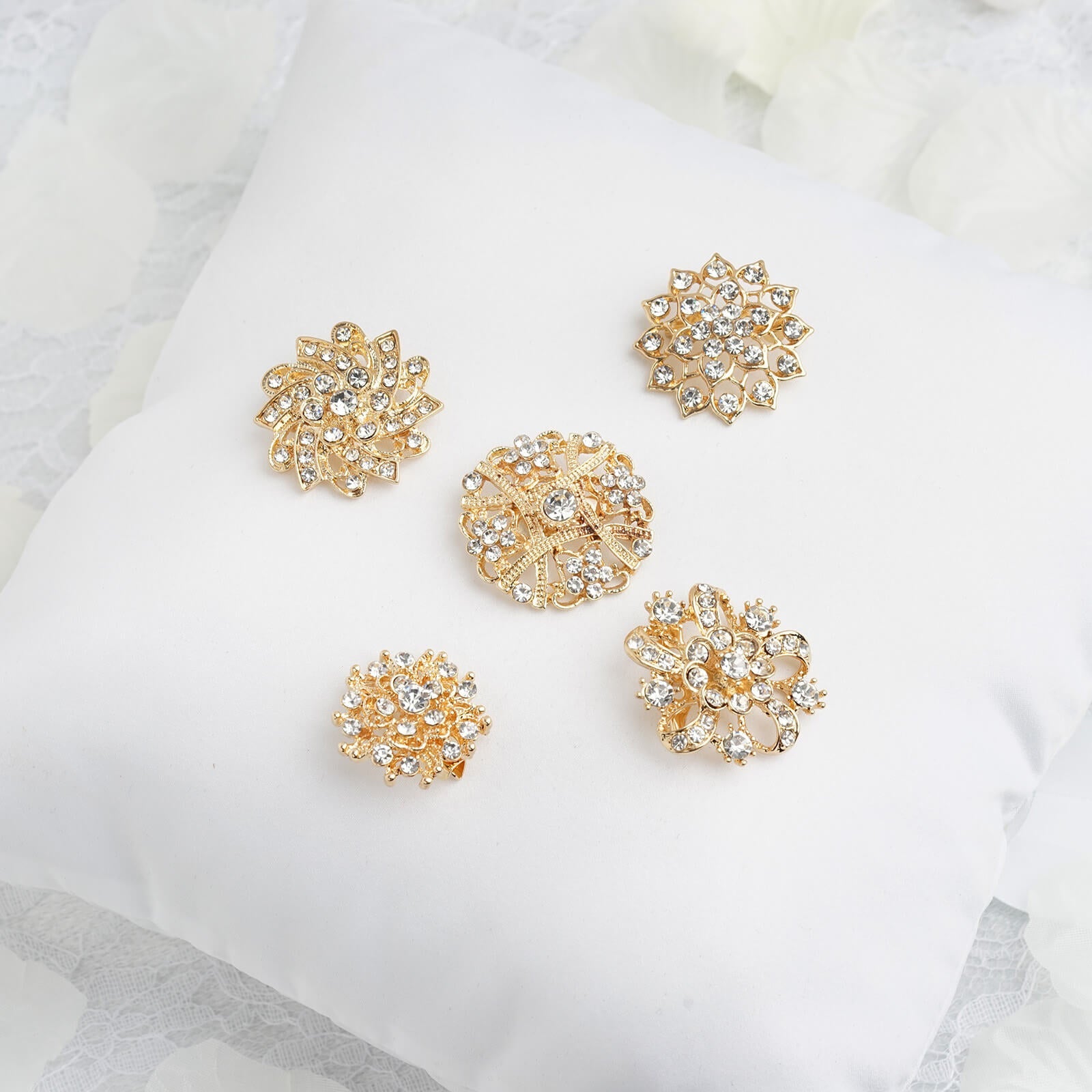 Gold plated mandala crystal rhinestone brooches on a white cushion.