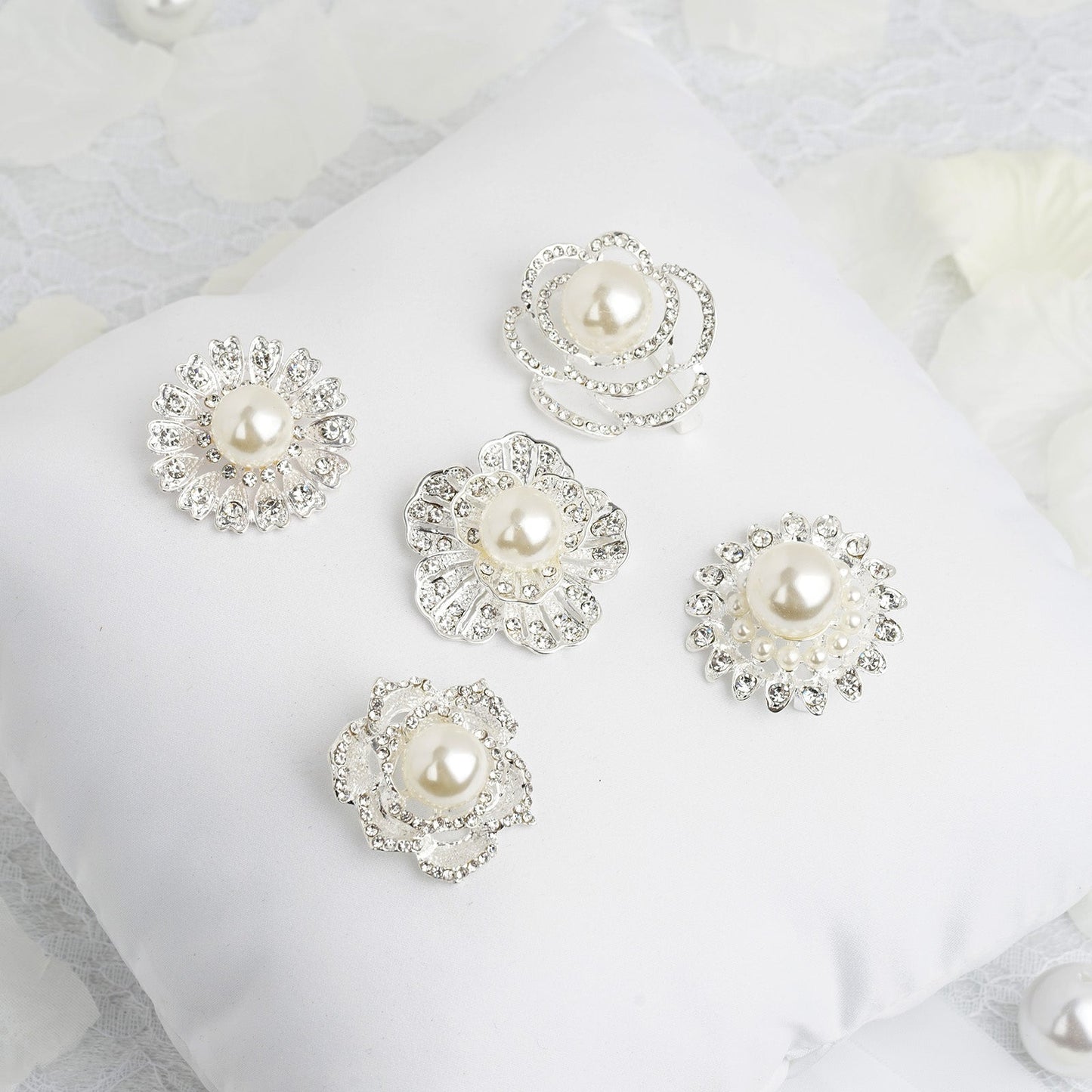 Assorted silver plated rhinestone brooches with pearl centers on a white cushion.
