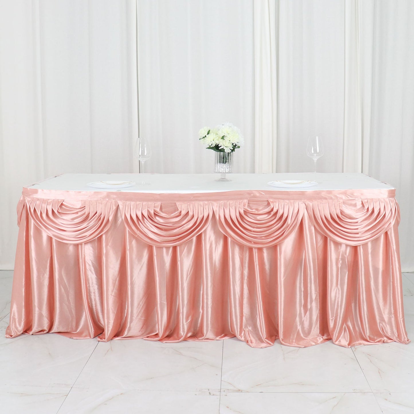 Dusty rose pleated satin table skirt draped elegantly on a table.