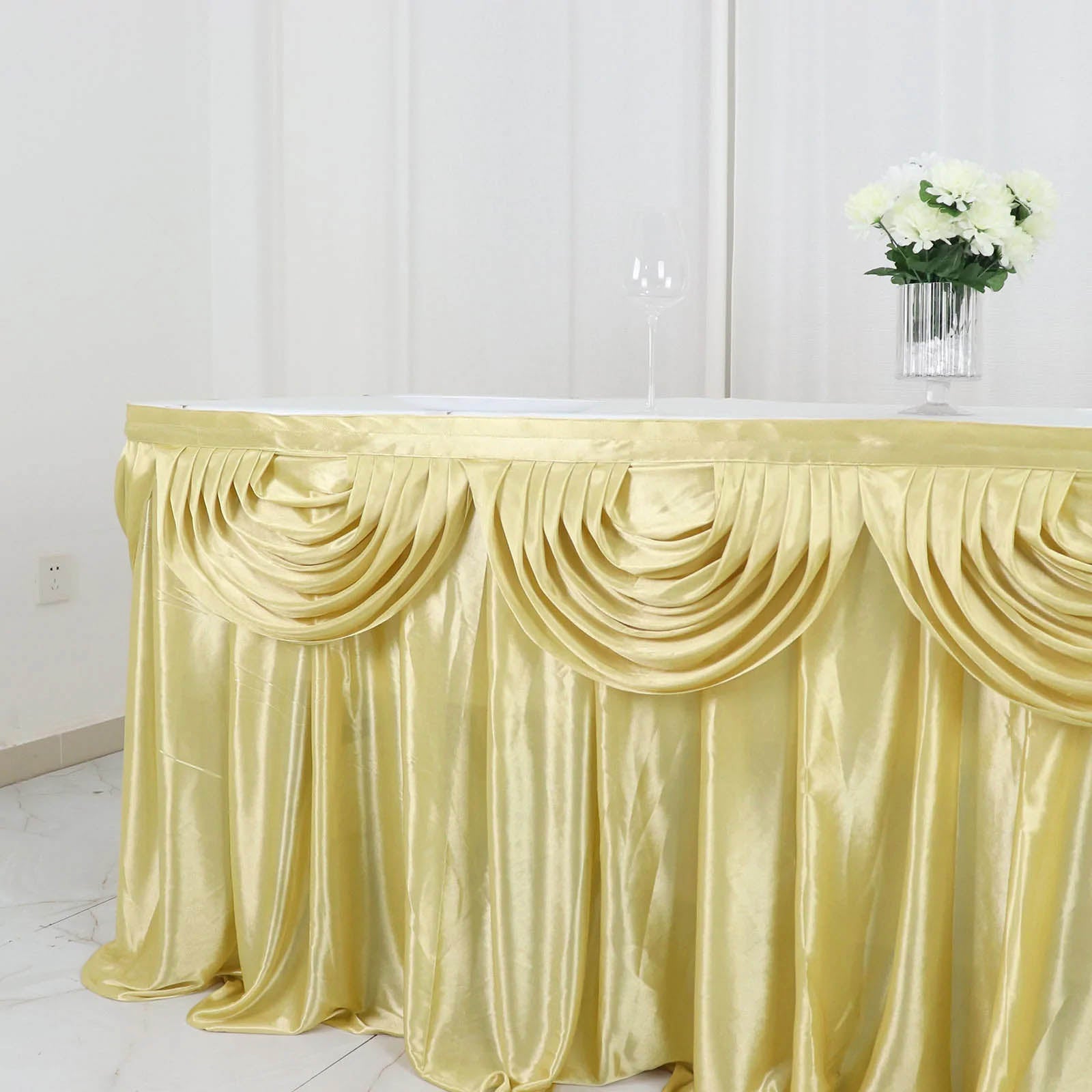 Champagne pleated satin table skirt draped elegantly on a table.