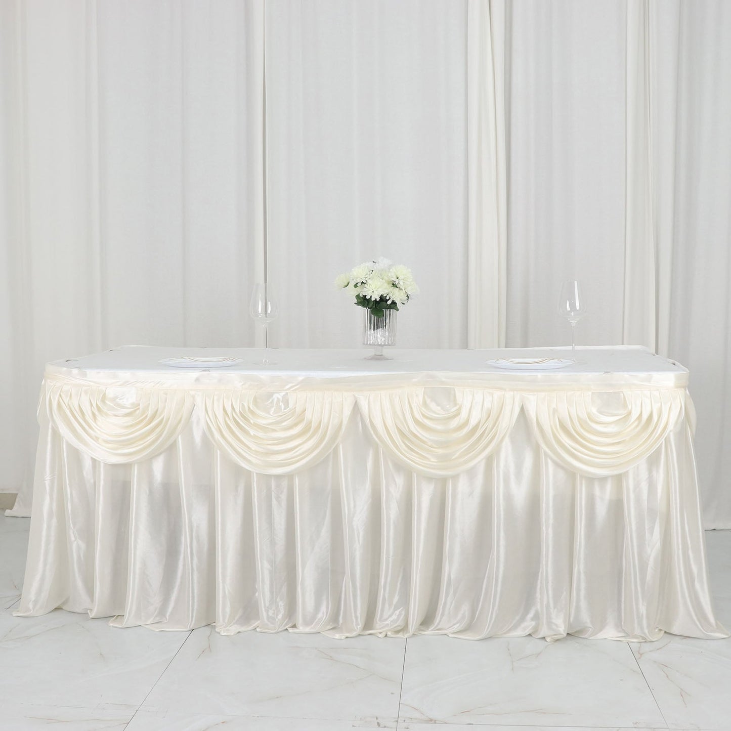 Ivory pleated satin double drape table skirt on a table with flowers.