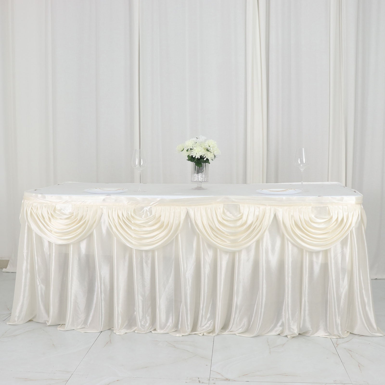 Ivory pleated satin double drape table skirt on a table with flowers.