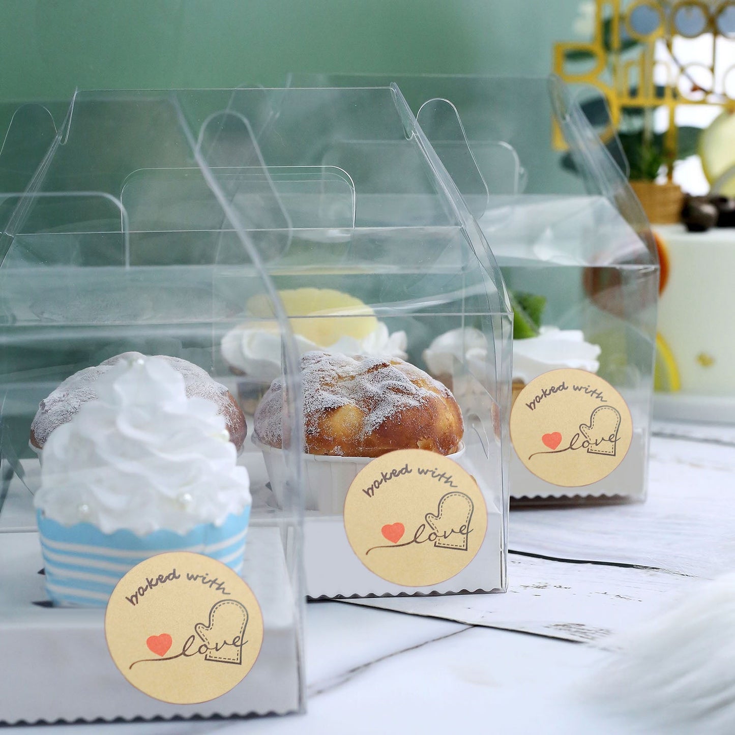 Baked with love stickers on clear bakery boxes with cupcakes and pastries.