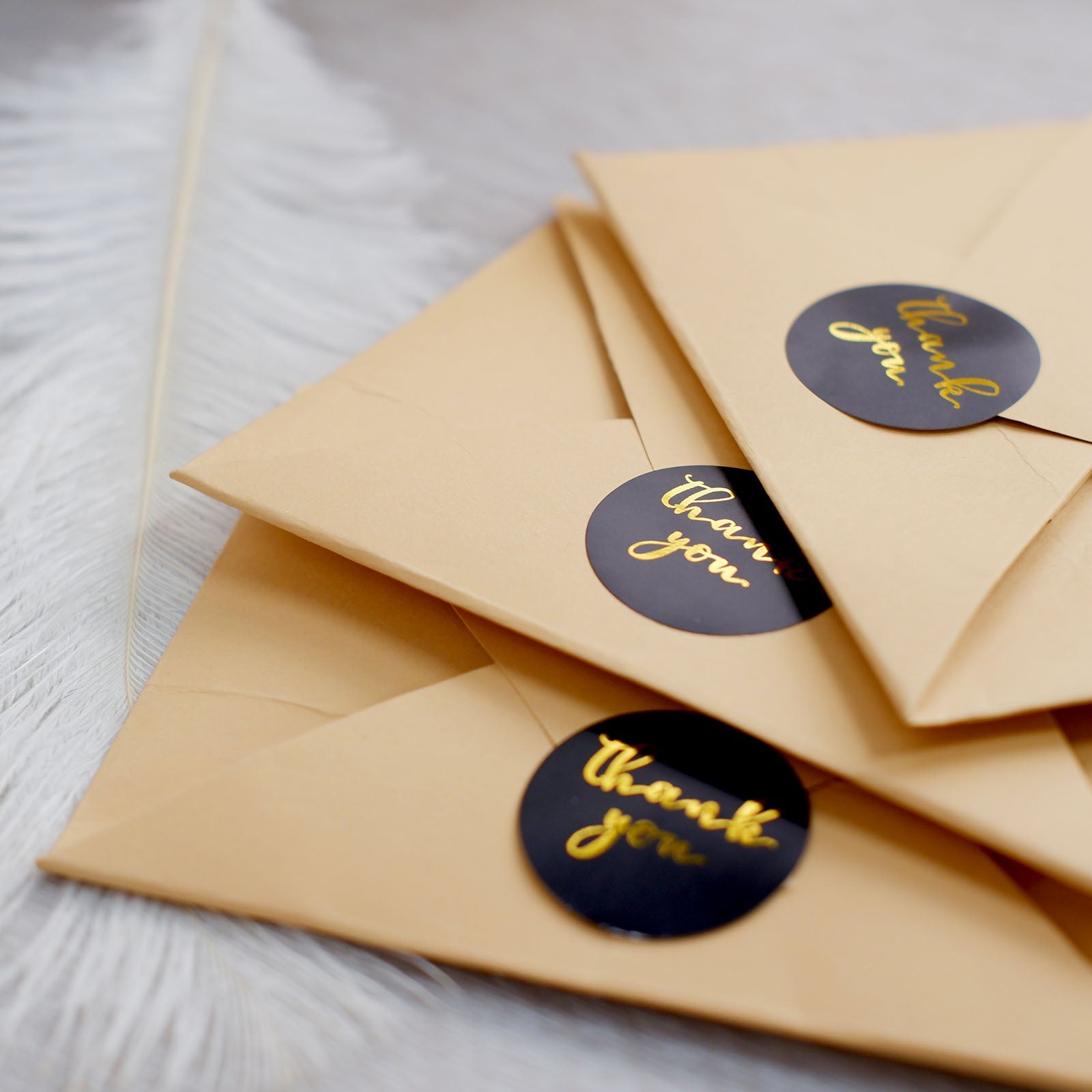 Black stickers with gold foil text on brown envelopes.