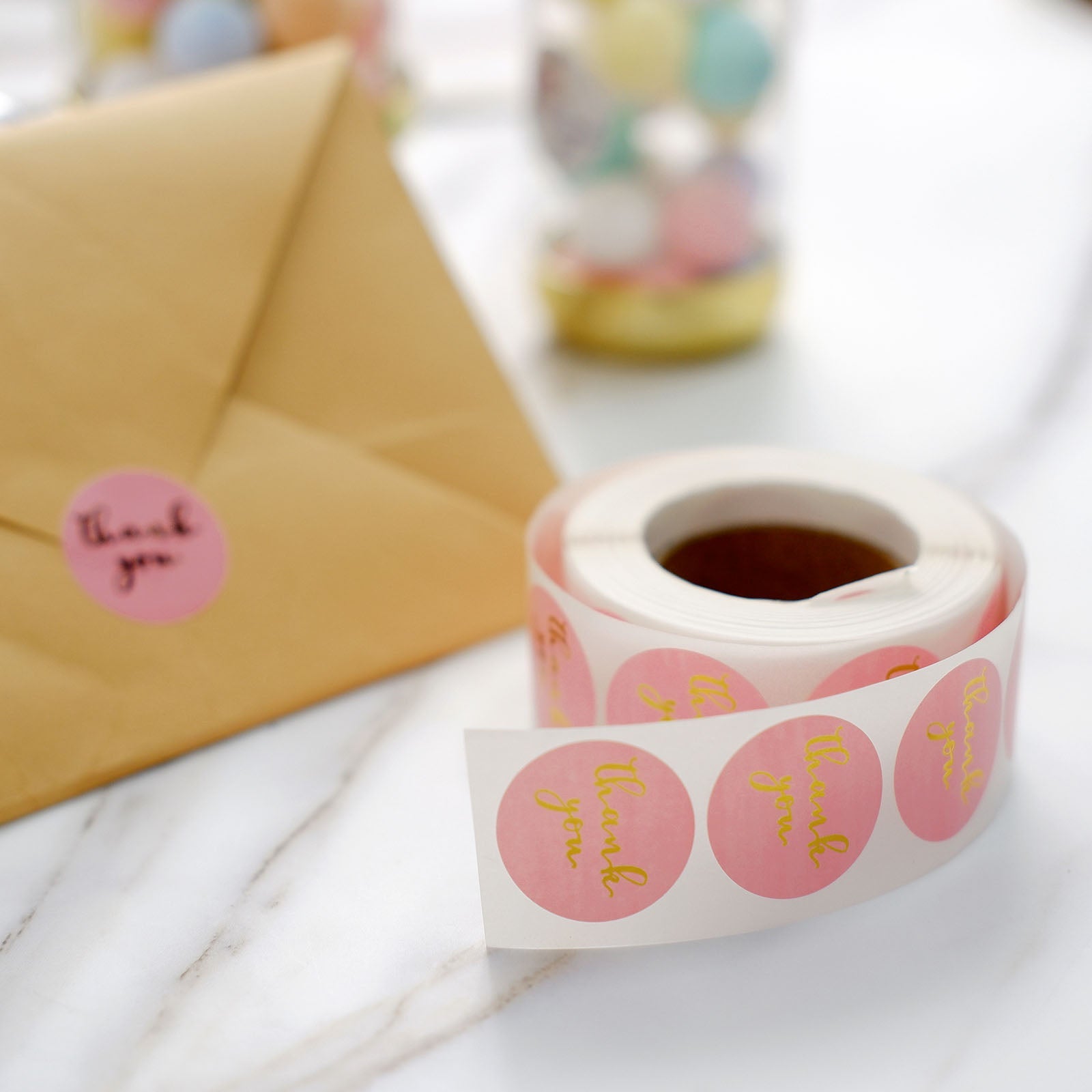 Gold foil "Thank You" stickers on pink roll for DIY envelopes.