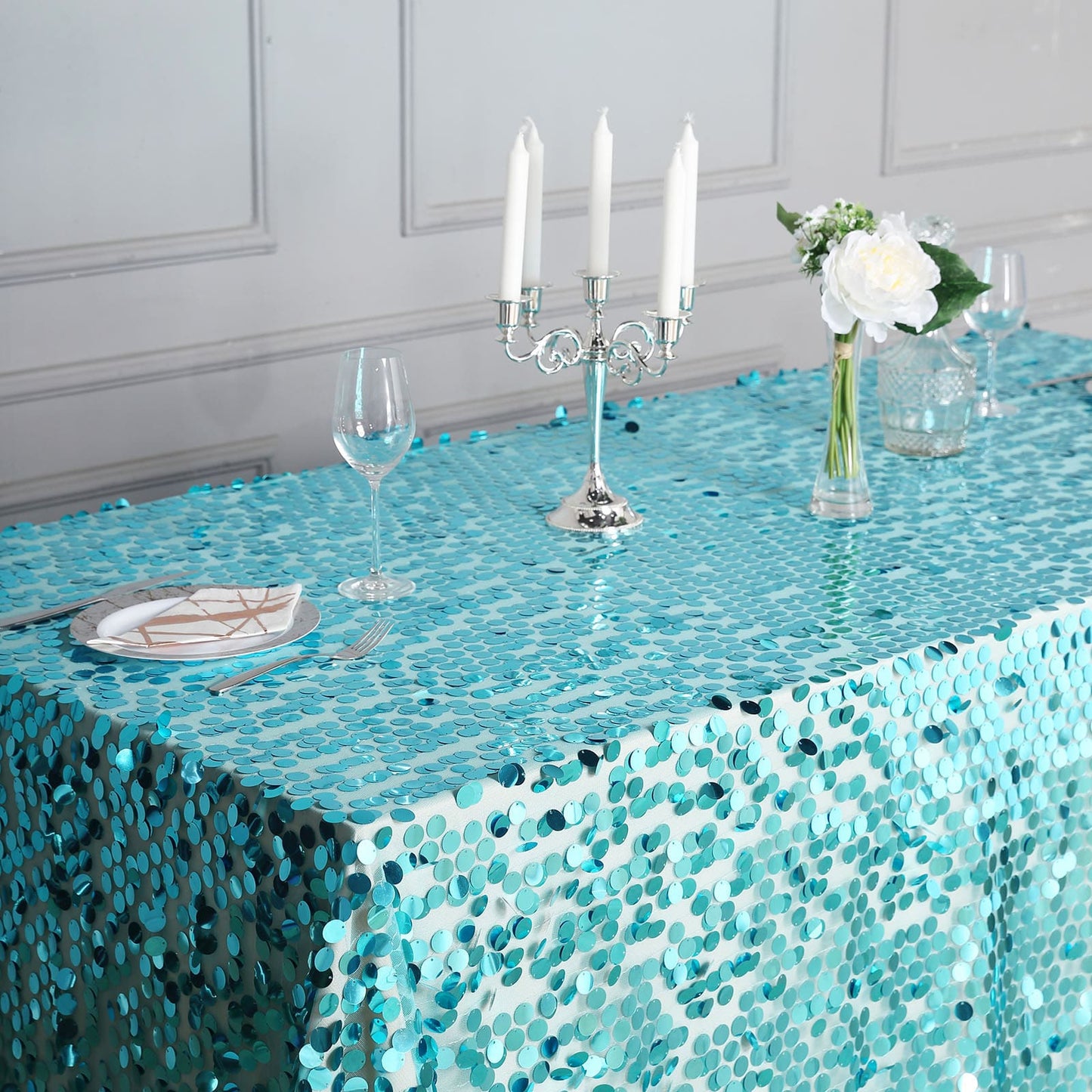 Turquoise sequin tablecloth on a dining table with candles and flowers.