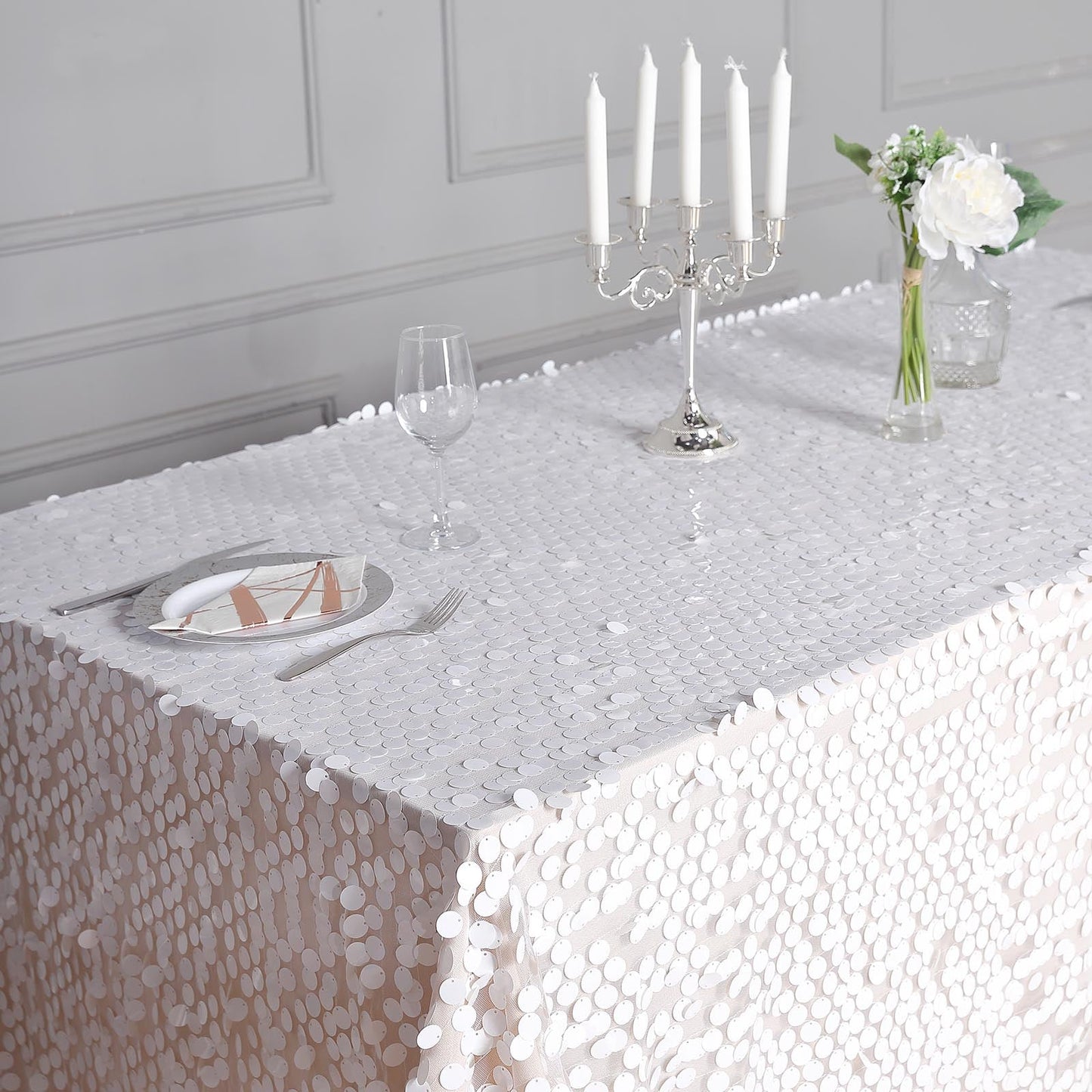 White sequin tablecloth on a dining table with candles and flowers.