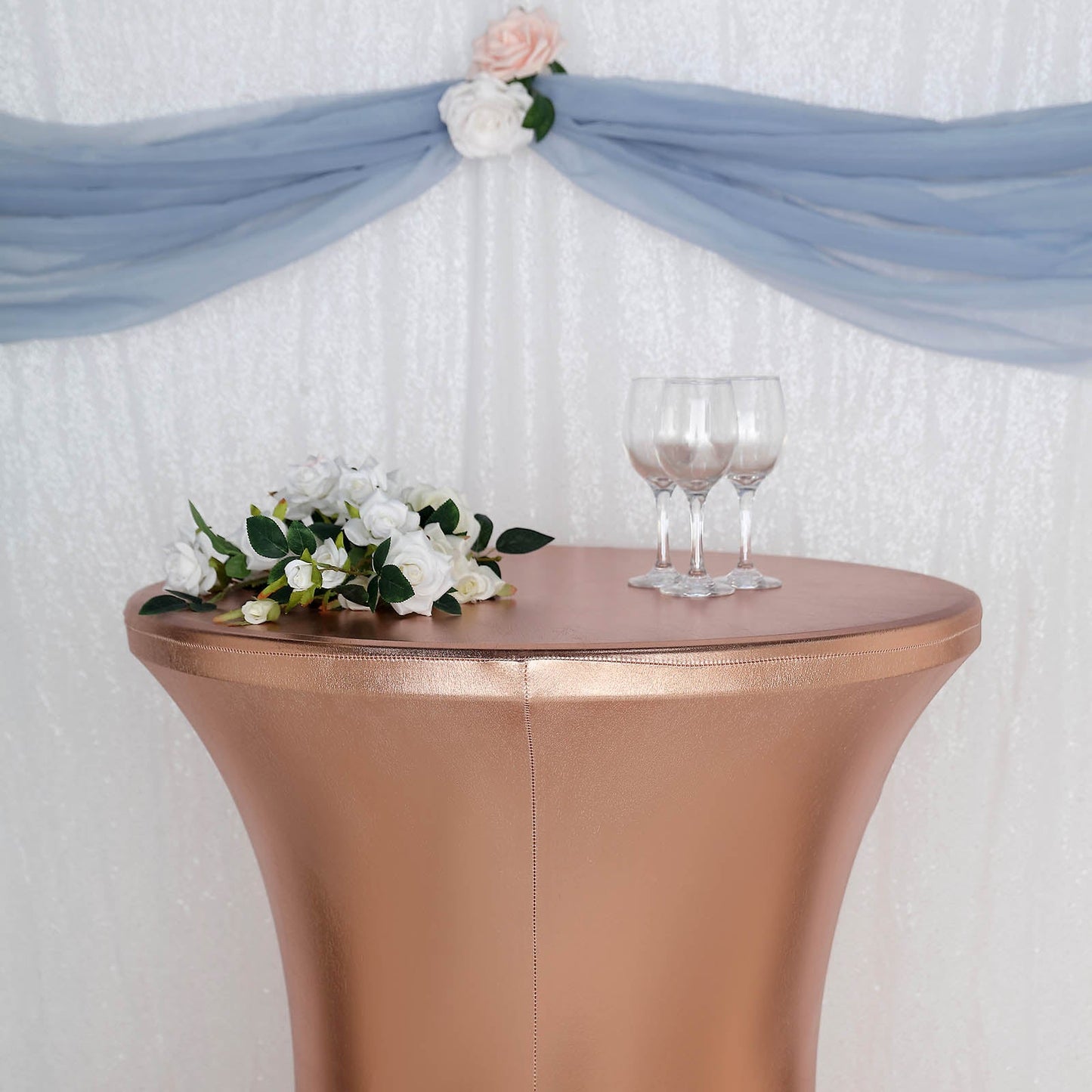 Blush metallic spandex fitted round cocktail table cover on a highboy table.