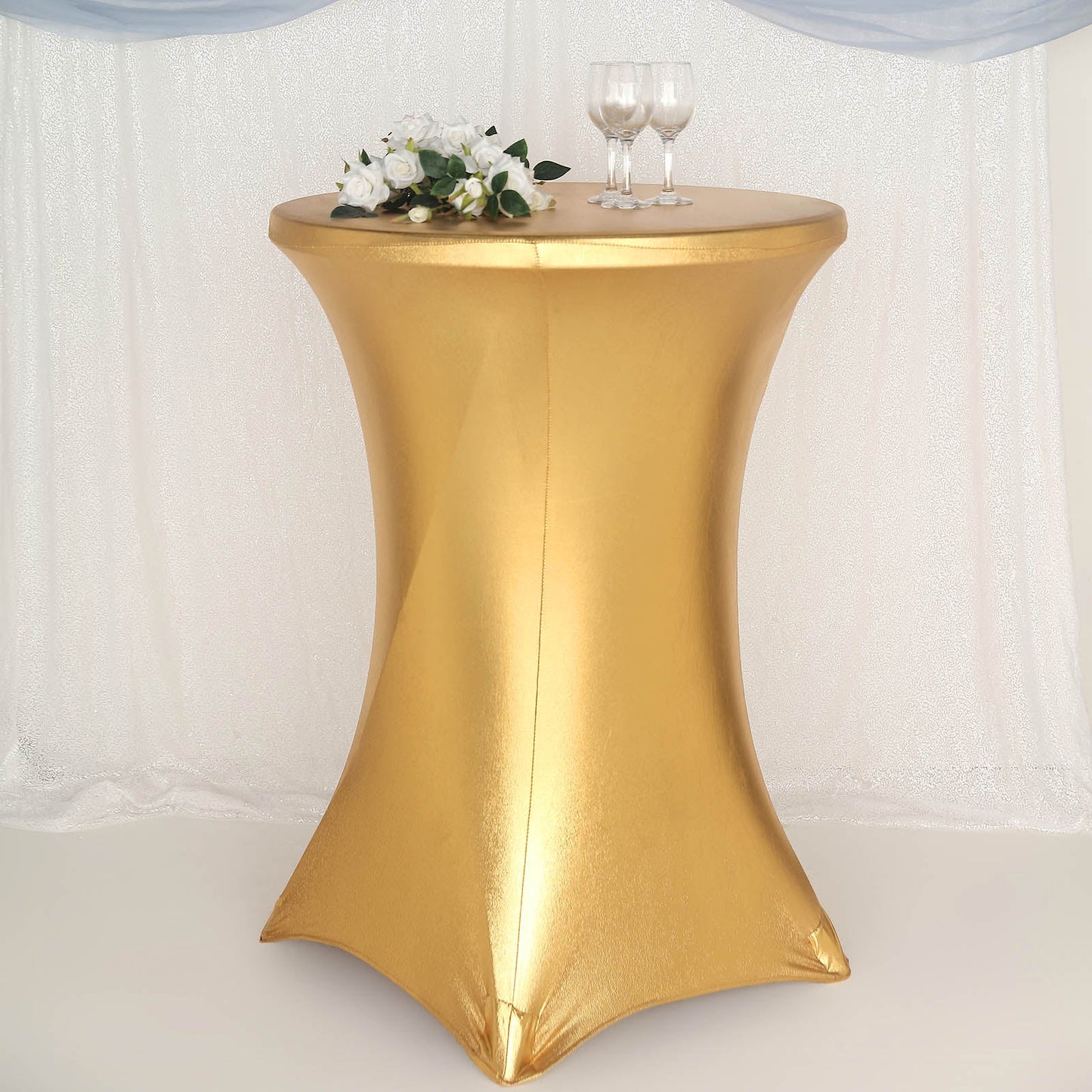 Gold fitted round cocktail table cover on a highboy table.