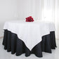 White square cotton table overlay on a round black table with red flowers.