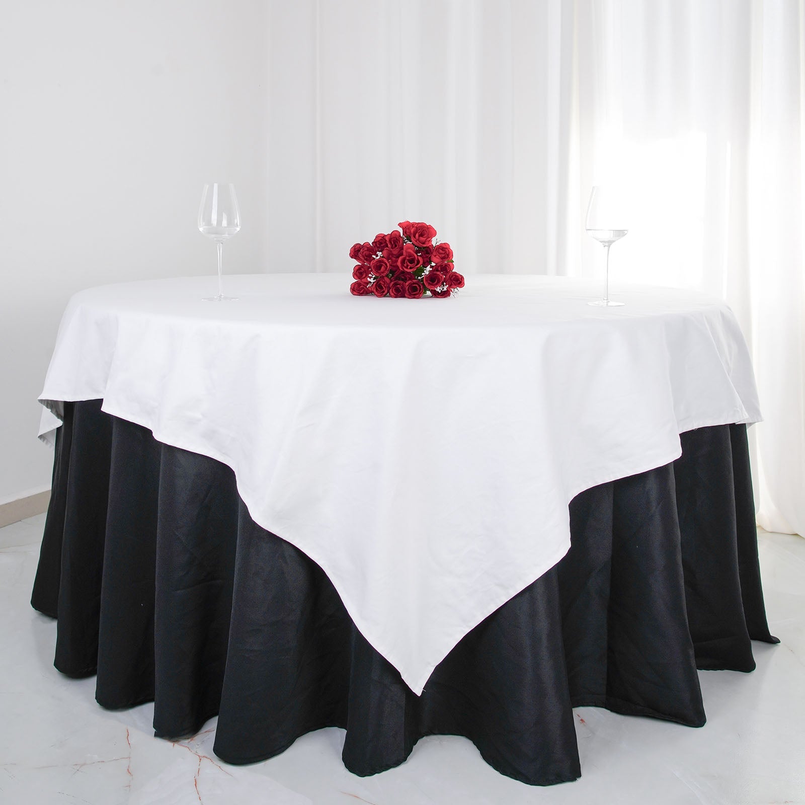 White square cotton table overlay on a round black table with red flowers.