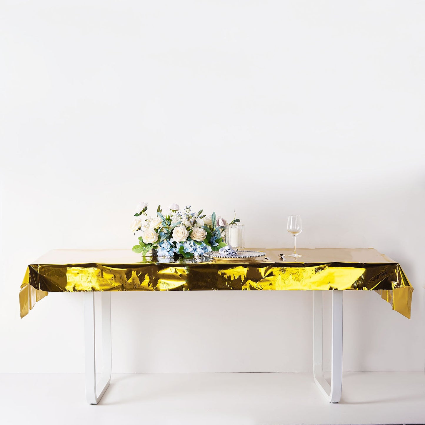 Gold metallic foil tablecloth on a table with floral arrangement and glass.