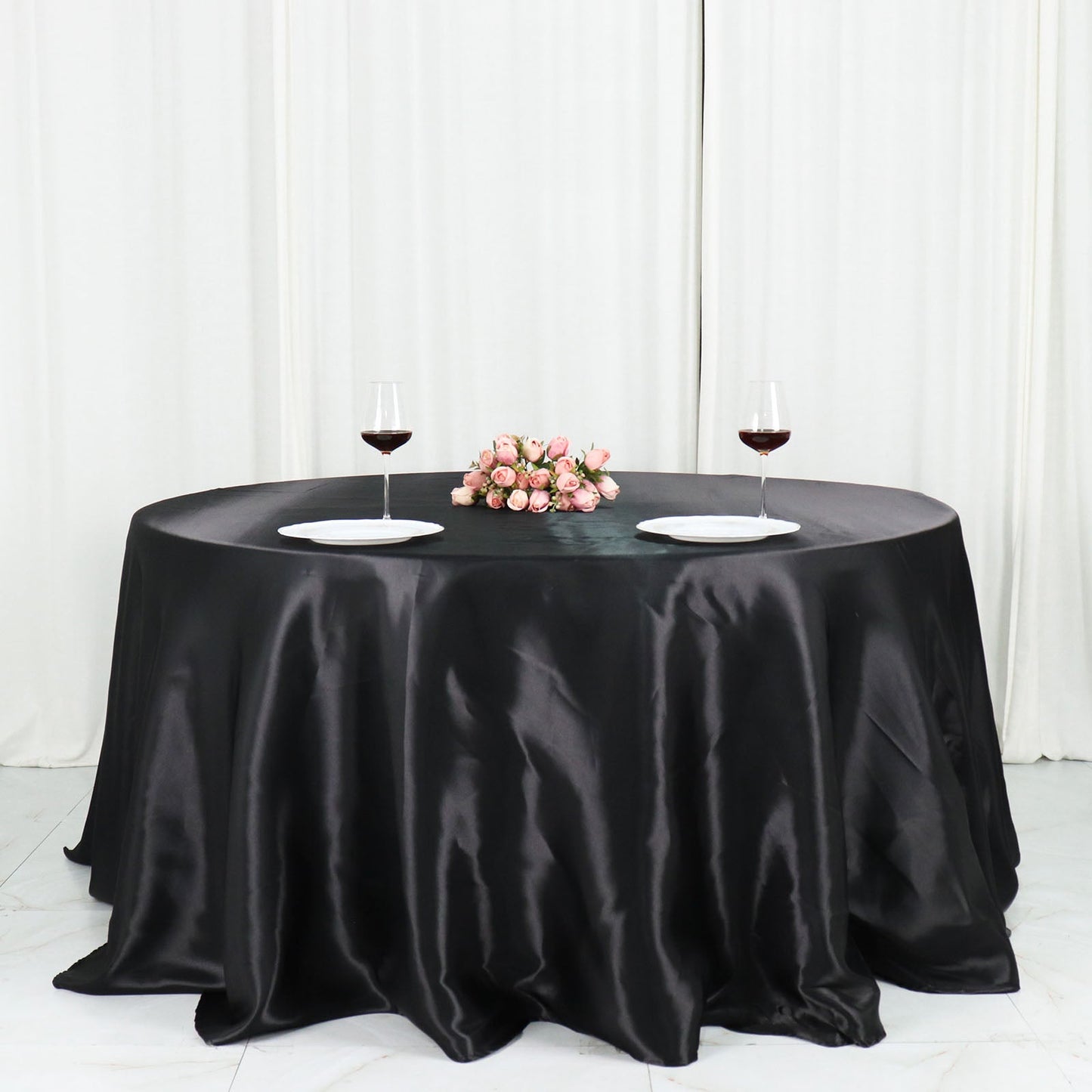Black satin round tablecloth on a dining table with wine glasses and flowers.