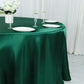 Emerald green satin round tablecloth on a dining table with plates and flowers.