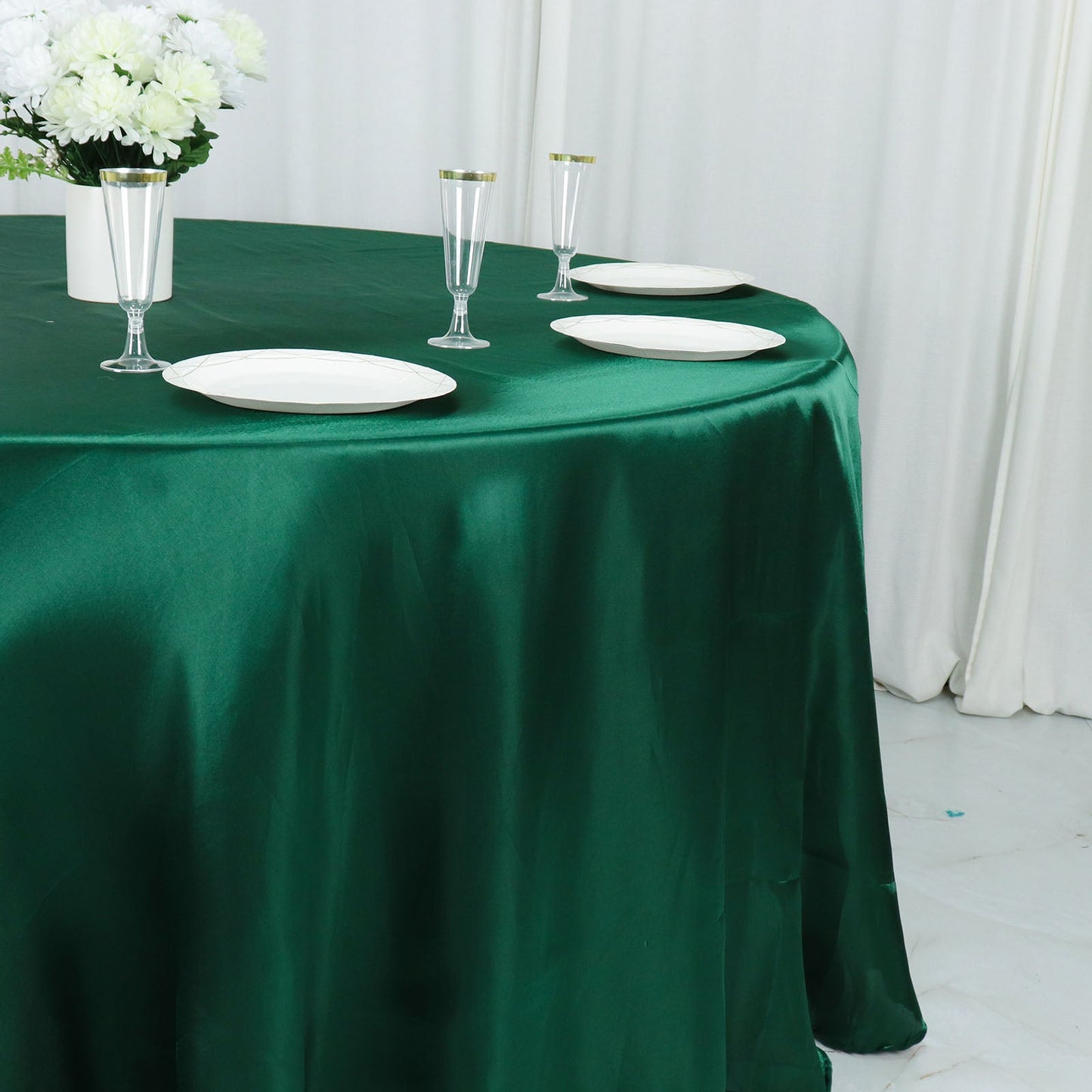 Emerald green satin round tablecloth on a dining table with plates and flowers.
