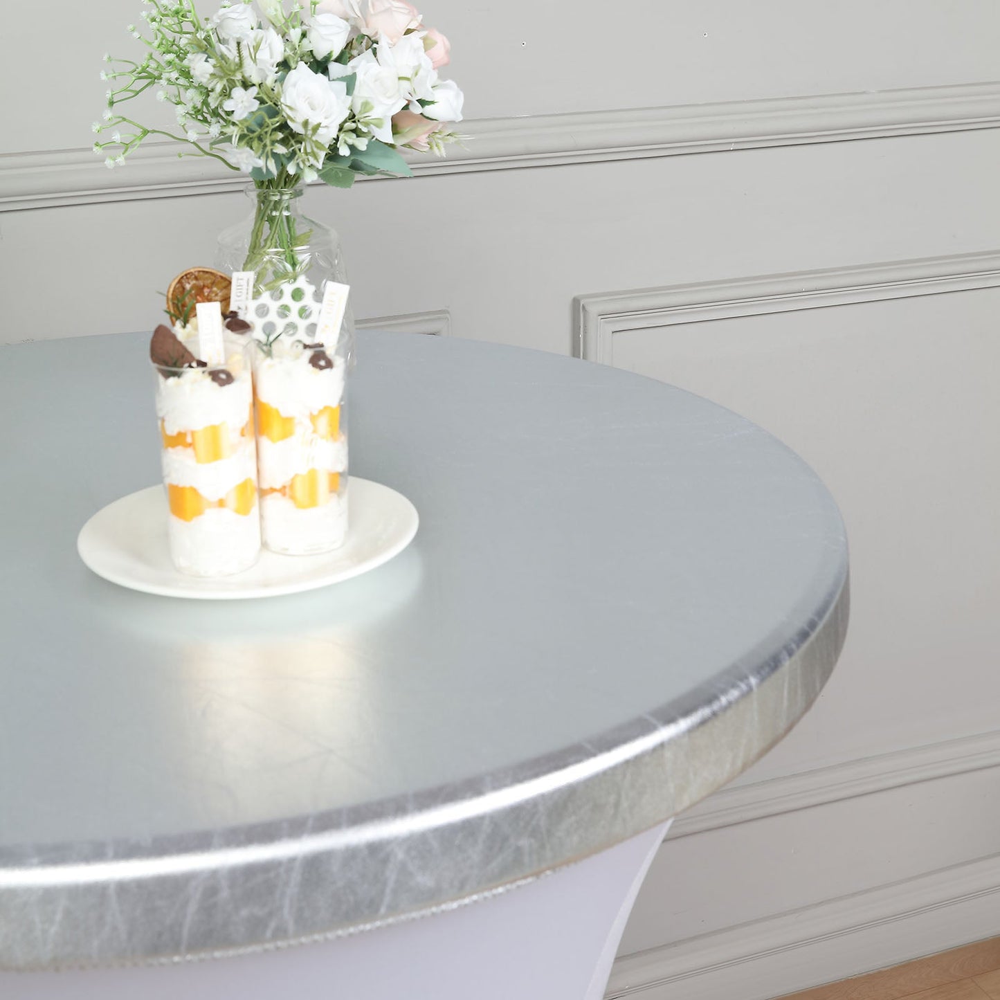 Metallic silver fitted cocktail table cover with desserts on top.