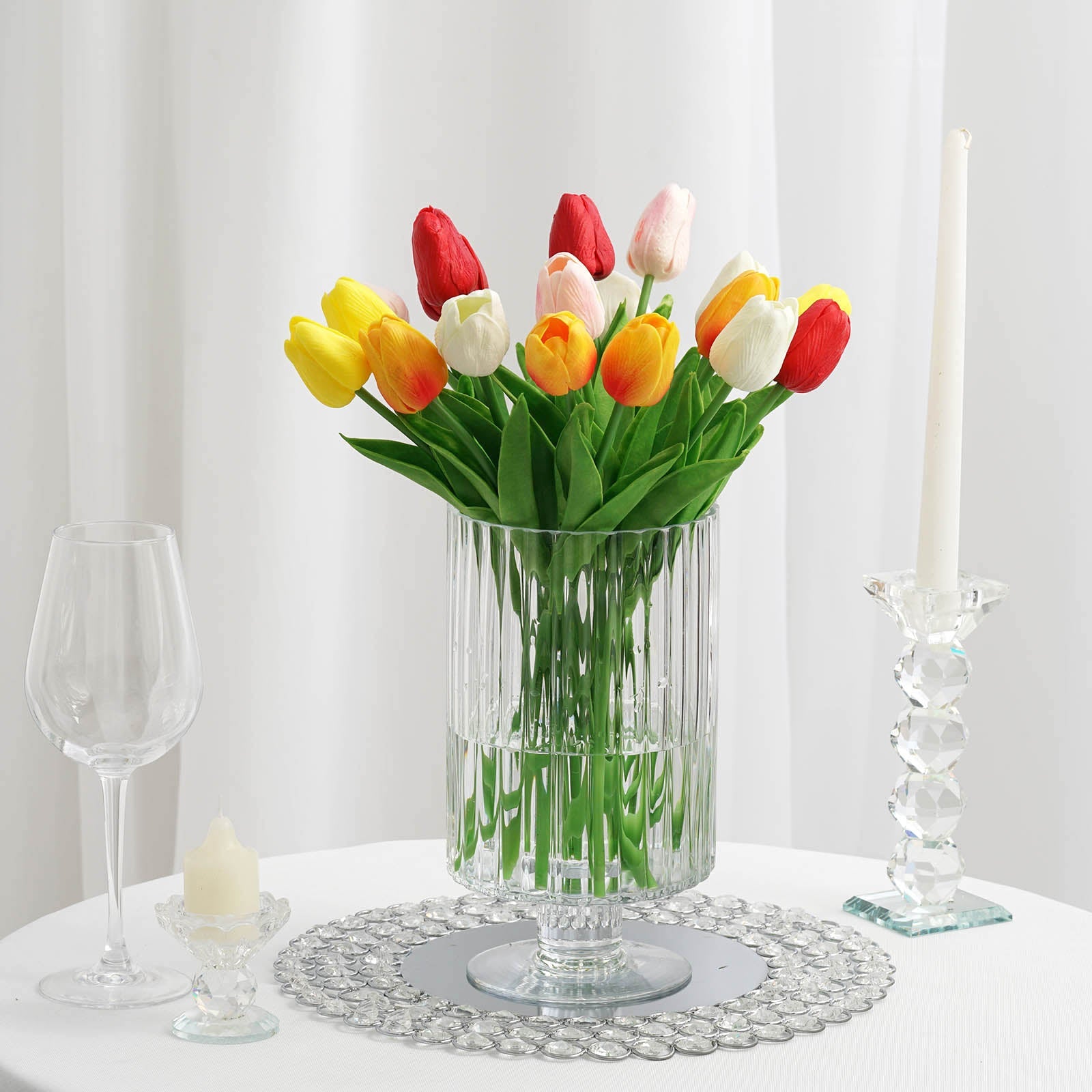 Clear ribbed glass vase with vibrant tulips and a candle holder.