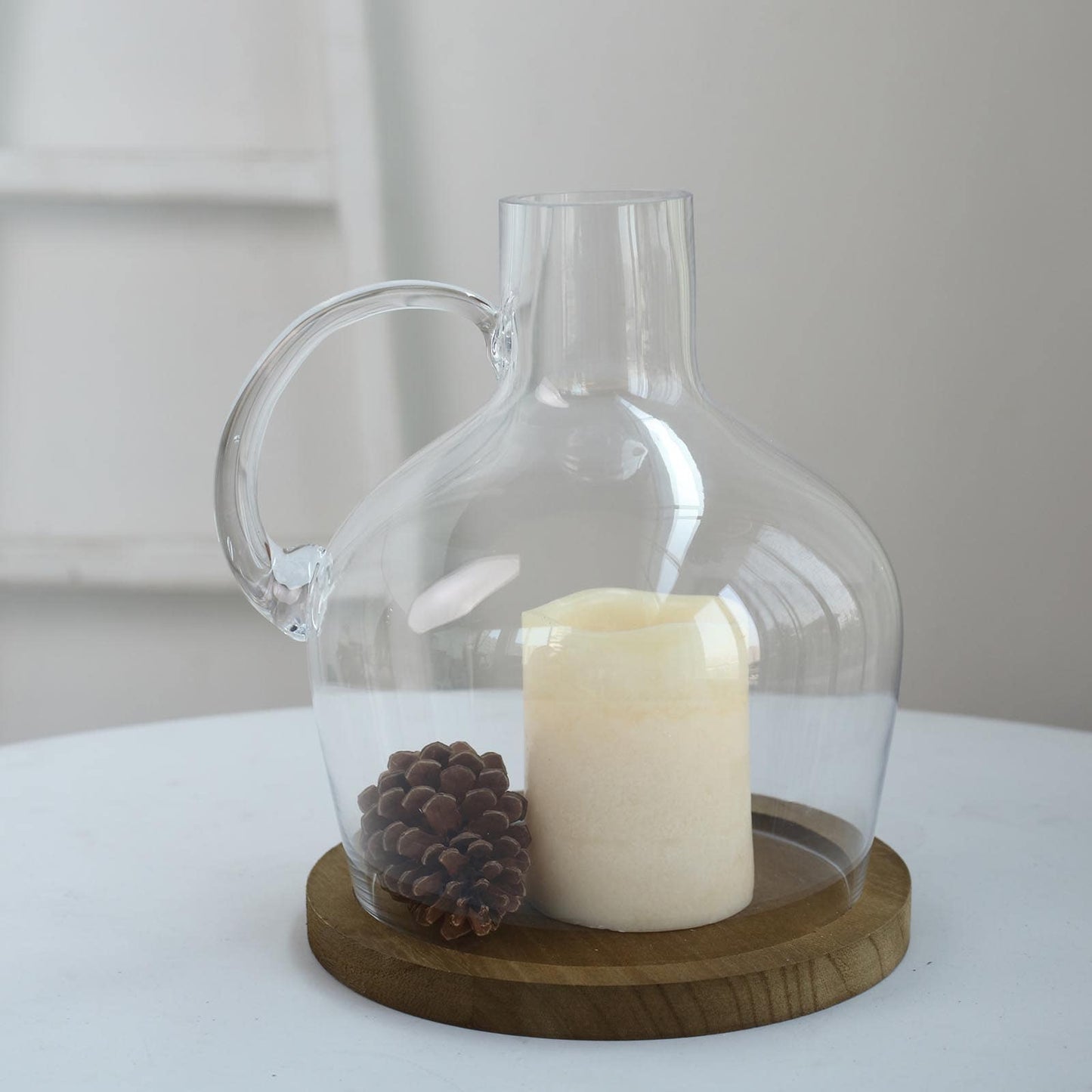 Clear glass vase with wooden base holding a candle and decorative pinecones.