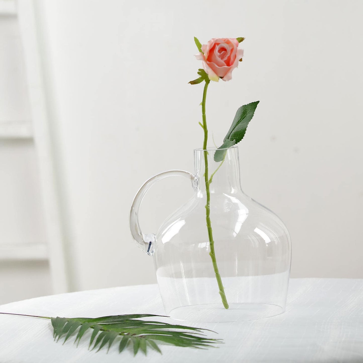 Clear glass vase with a pink rose and green leaves.