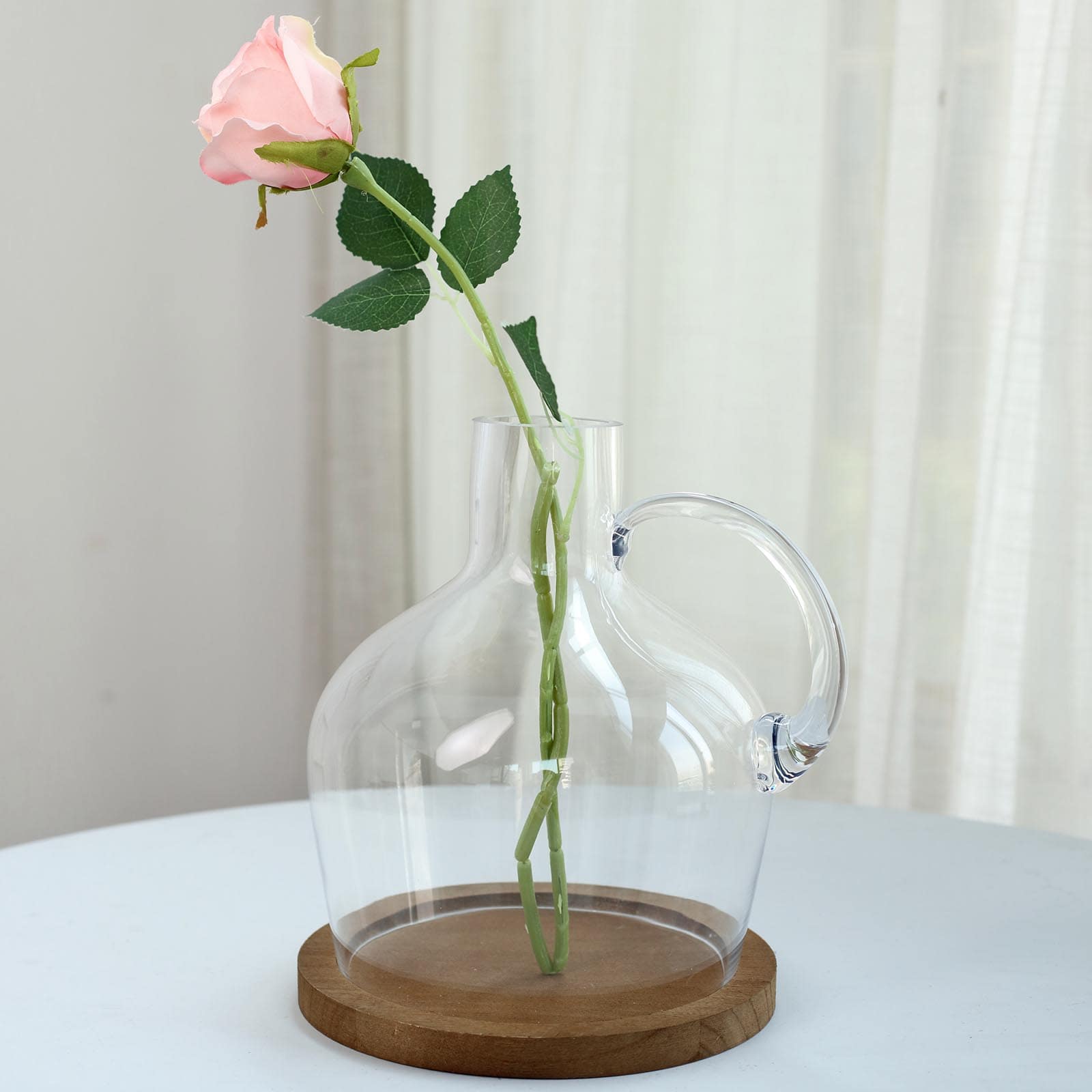 Clear glass vase with a pink rose on a wooden base.