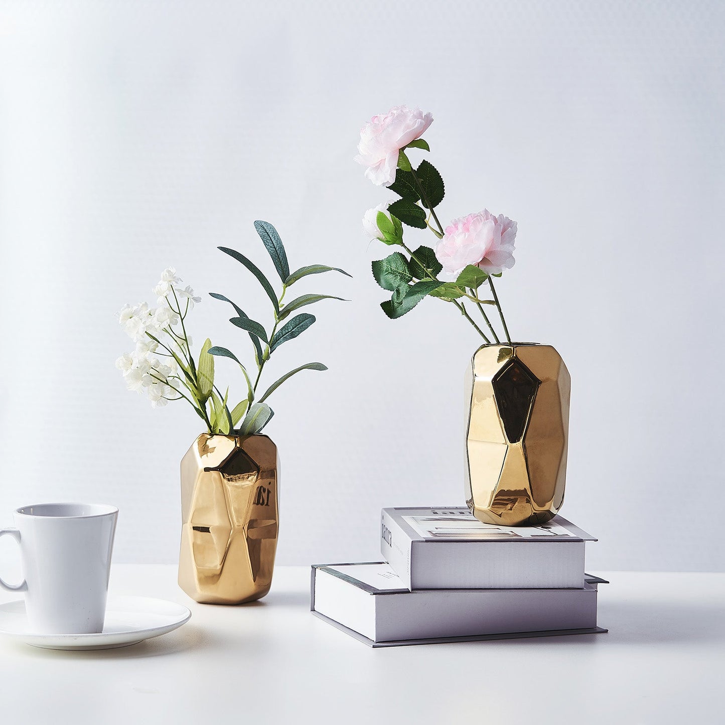 Gold metallic geometric ceramic vases with flowers on stacked books.