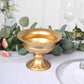 Gold metal flower pedestal vase on a table with greenery and floral accents.