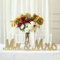 Gold glittered "Mr & Mrs" table display with flowers in a rustic wedding setting.
