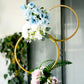 Gold metal hoop flower stand with blue and white floral arrangement.