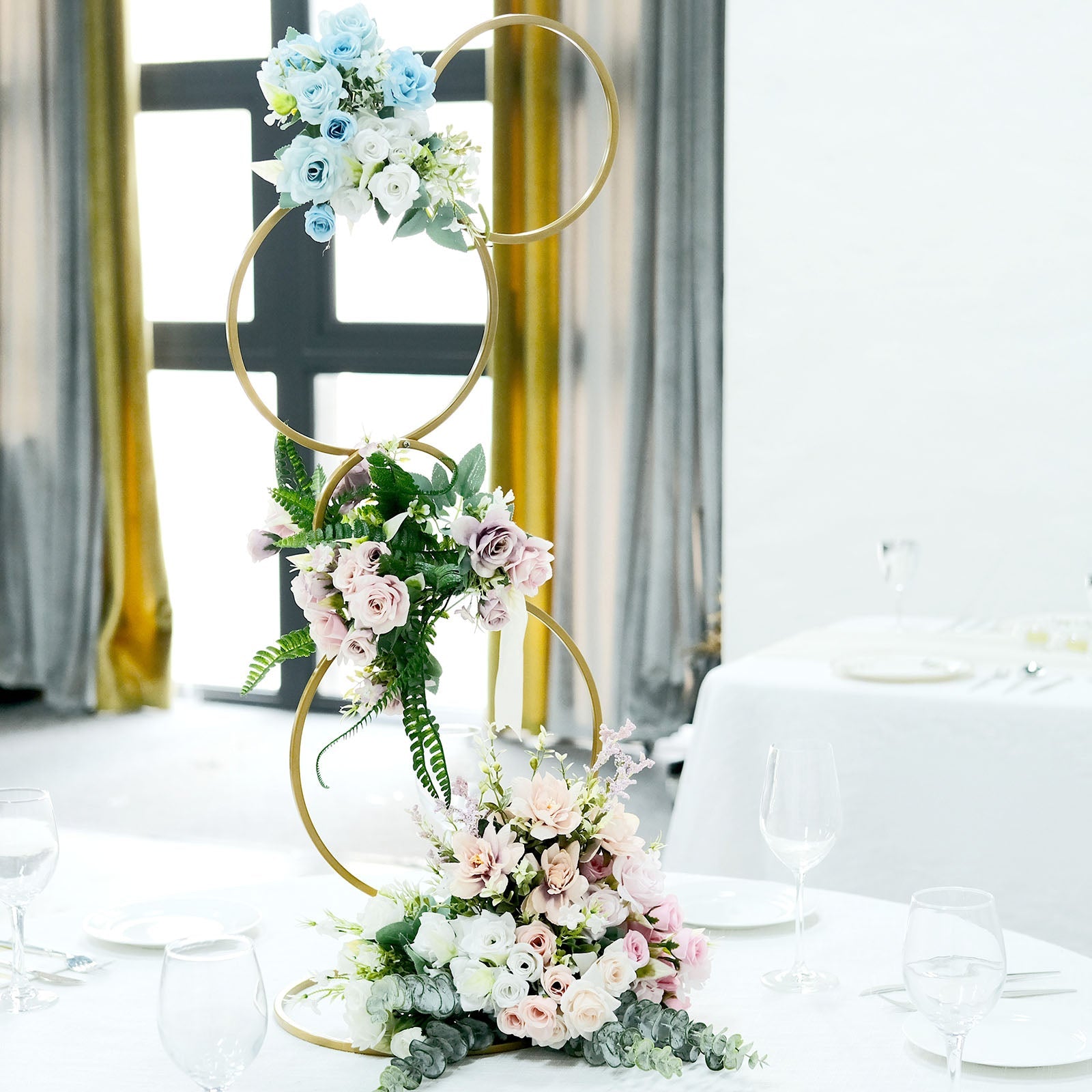 Gold metal hoop pillar flower stand with pastel floral arrangements.
