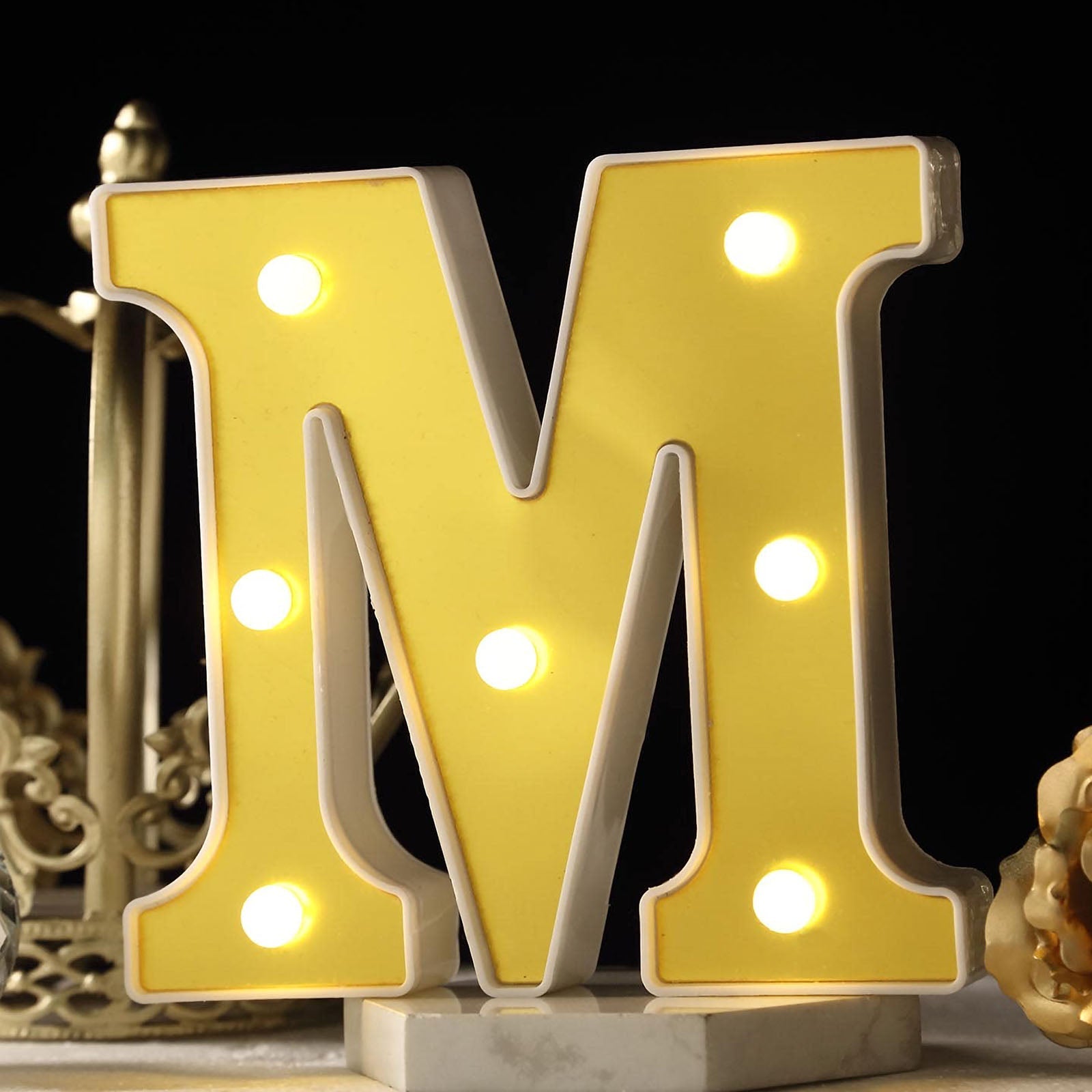 Gold 3D marquee letter "M" with warm white LED lights.