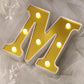 Gold 3D marquee letter "M" with warm white LED lights.