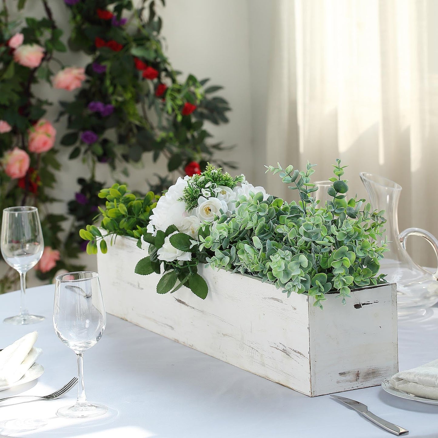 White rectangular wood planter box with removable liners, filled with greenery and flowers.