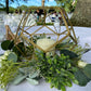 Gold metal geometric tealight candle holder surrounded by greenery.