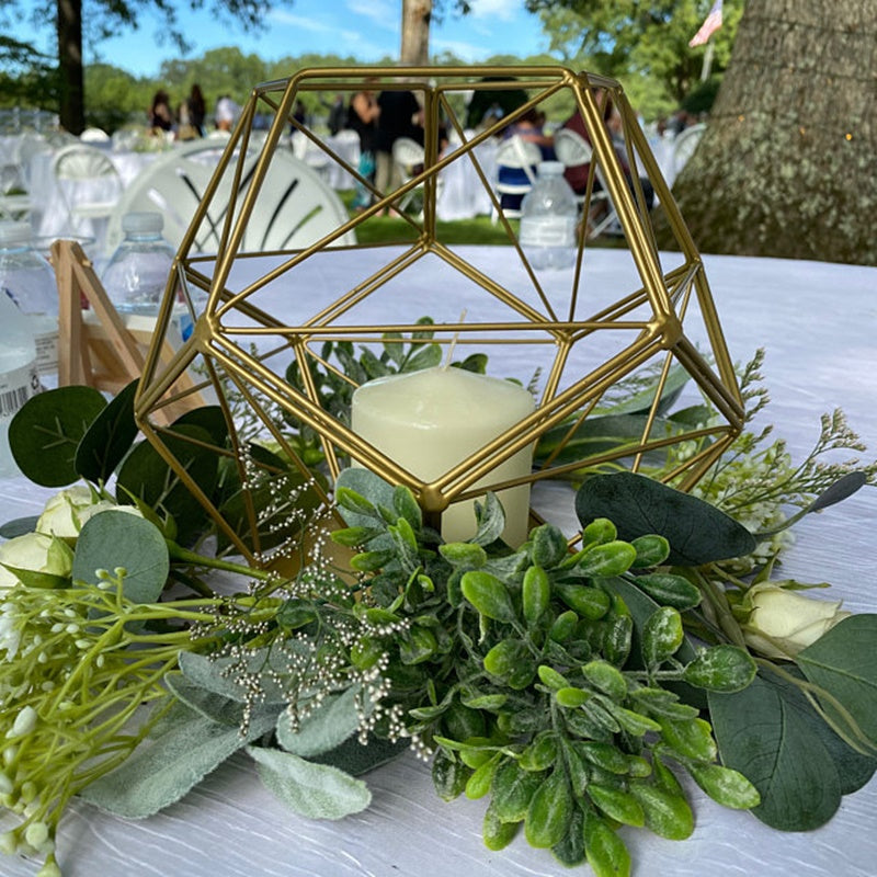Gold metal geometric tealight candle holder surrounded by greenery.